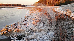 Low flight over the orange shore of a reservoir with frosty vegetation