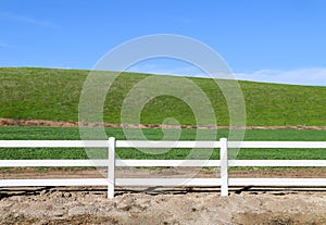 Low grassland hillside hills pasture with bright sunny blue sky and wooden white picket farm livestock fence