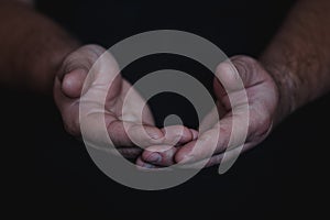 Low key, close up of hands of a faithful mature man praying, hands folded, interlaced fingers in worship to god