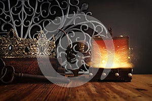 low key image of beautiful queen or king crown over antique book next to wooden treasure chest. vintage filtered. fantasy medieval
