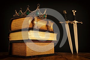 low key image of beautiful queen/king crown over antique book and sword. fantasy medieval period. Selective focus