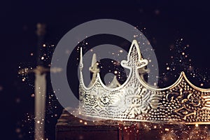 low key image of beautiful queen/king crown over antique box next to sword. fantasy medieval period. Selective focus. Glitter