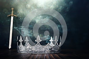 low key image of beautiful queen or king crown over antique next to sword. fantasy medieval period. Selective focus. Glitter