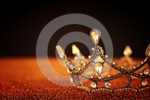 low key image of beautiful queen/king crown over gold glitter table. vintage filtered. fantasy medieval period