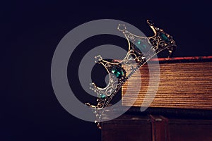 low key image of beautiful queen/king crown over old book and wooden table. vintage filtered. fantasy medieval period