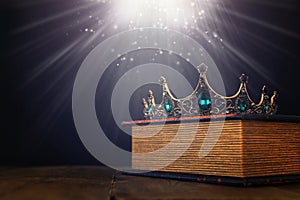 low key image of beautiful queen/king crown over old book and wooden table. vintage filtered. fantasy medieval period