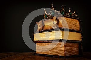 low key image of beautiful queen/king crown over old book and wooden table. vintage filtered. fantasy medieval period