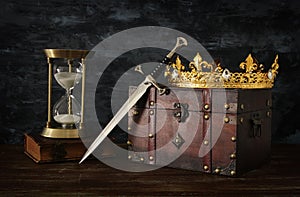 low key image of beautiful queen/king crown, vintage hourglass and sword. fantasy medieval period.