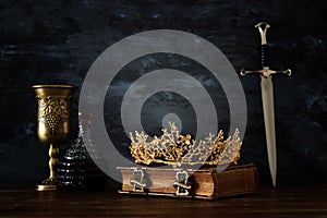 low key image of beautiful queen/king crown, wine cup and sword. fantasy medieval period.