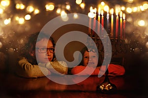 Low key image of jewish holiday Hanukkah background with two cute kids looking at menorah & x28;traditional candelabra& x29;