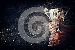 low key image of a man holding a trophy cup over dark background