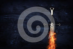 low key image of silver sword in the flames of fire. fantasy medieval period.