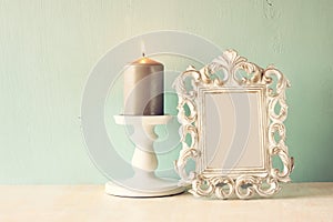 Low key image of vintage antique classical frame and Burning candle on wooden table. filtered image.