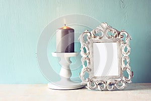 Low key image of vintage antique classical frame and Burning candle on wooden table. filtered image