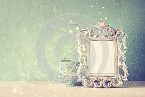 Low key image of vintage antique classical frame and wooden table and glitter lights background. filtered image.