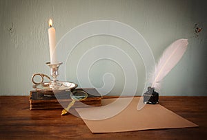 Low key image of white Feather, inkwell, burning Candle and ancient book on wooden table. filtered image