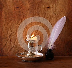 Low key image of white Feather, inkwell and burning candle on a wooden table