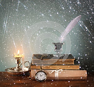 Low key image of white Feather, inkwell, old books and candle and glitter lights background on old wooden table