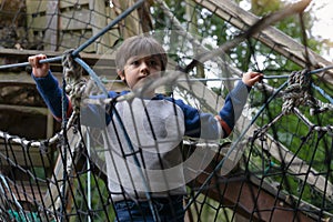 Low key light Portrait active kid climbing on rope frame at treehouse in the park. A boy standing alone on rope bridge in
