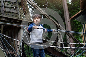 Low key light Portrait active kid climbing on rope frame at treehouse in the park. A boy standing alone on rope bridge in