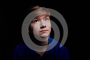 Low key portrait of a handsome brunette young male teenager in blue t-shirt. Interesting boy and dark background with blue light