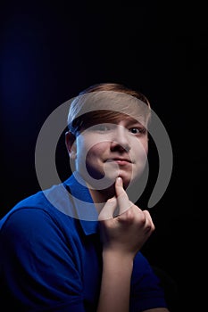 Low key portrait of a handsome brunette young male teenager in blue t-shirt. Interesting boy and dark background with blue light