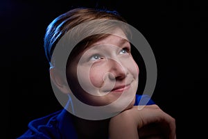 Low key portrait of a handsome brunette young male teenager in blue t-shirt. Interesting boy and dark background with blue light