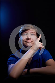 Low key portrait of a handsome brunette young male teenager in blue t-shirt. Interesting boy and dark background with blue light