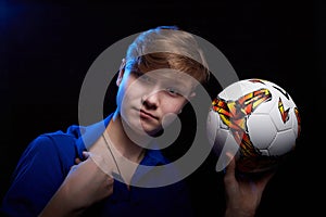 Low key portrait of a handsome brunette young male teenager in blue t-shirt with soccer ball in his hand. Interesting boy soccer