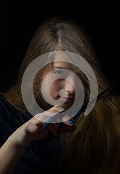 Low-key young girl ironic portrait cutting hair with scissors