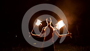 Low key. Young male with long hair and bare torso rotates burning torch outdoors on a black night video slow motion