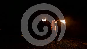 Low key. Young male with long hair and bare torso rotates burning torch outdoors on a black night video slow motion