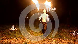 Low key. A young male with long hair and a naked torso rotates a burning torch outdoors on a black night video slow