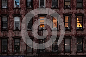 Low light night time view of a red  brick face building in Manhattan, New York City. Lights glow warmly through one set of apartme