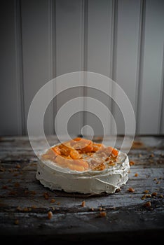 Low light photo of home made carrot cake with cream cheese frosting, fresh oranges and caramel crumbles