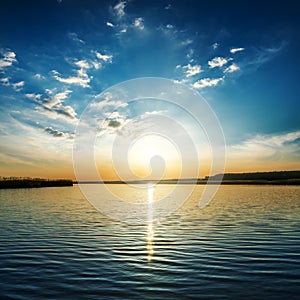 Low orange sun in clouds over river