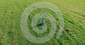 Low orbital flight around man on green grass with notebook pad at yellow rural field.