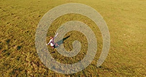 Low orbital flight around man on green grass with notebook pad at yellow rural field.