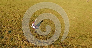 Low orbital flight around man on green grass with notebook pad at yellow rural field.