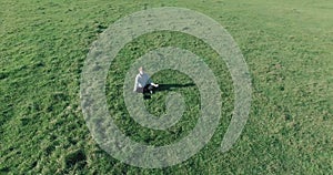 Low orbital flight around man on green grass with notebook pad at yellow rural field.