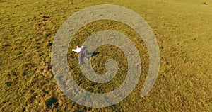 Low orbital flight around man on green grass with notebook pad at yellow rural field.