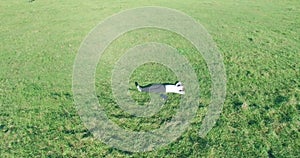 Low orbital flight around man on green grass with notebook pad at yellow rural field.
