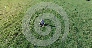 Low orbital flight around man on green grass with notebook pad at yellow rural field.