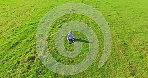 Low orbital flight around man on green grass with notebook pad at yellow rural field.