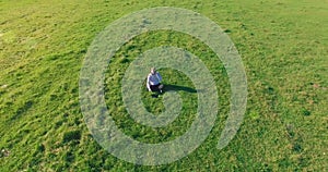 Low orbital flight around man on green grass with notebook pad at yellow rural field.