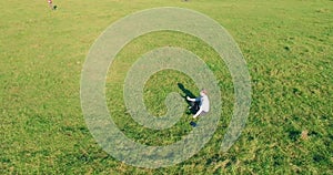 Low orbital flight around man on green grass with notebook pad at yellow rural field.