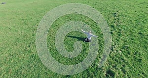 Low orbital flight around man on green grass with notebook pad at yellow rural field.