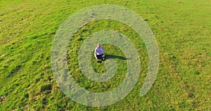 Low orbital flight around man on green grass with notebook pad at yellow rural field.