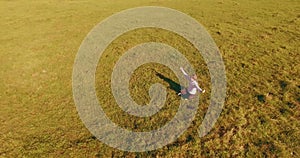 Low orbital flight around man on green grass with notebook pad at yellow rural field.