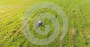 Low orbital flight around man on green grass with notebook pad at yellow rural field.